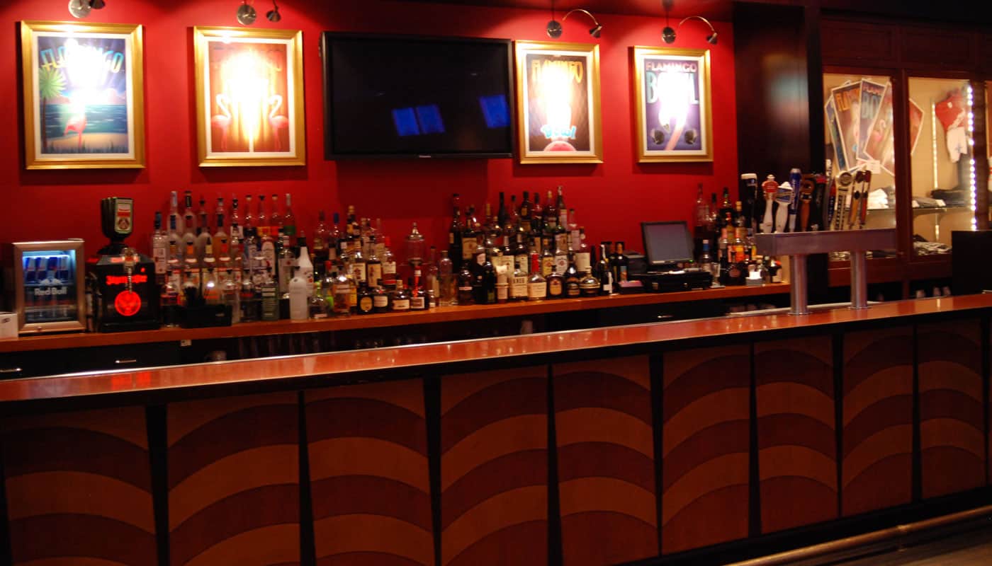 The full bar with backlit liquor shelves and framed art on red walls