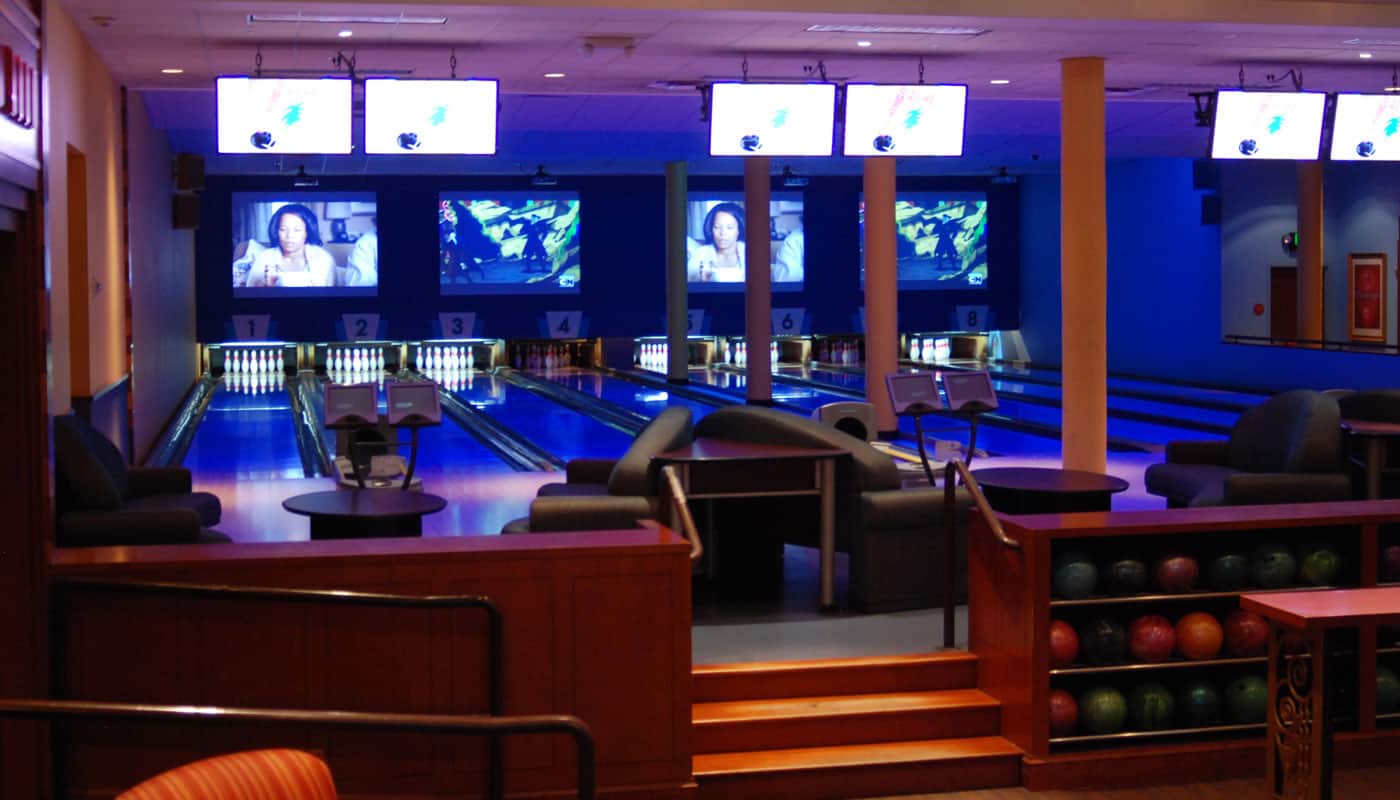 Eight bowling lanes in the Main Room lit in blue and purple, with a rack of colorful bowling balls