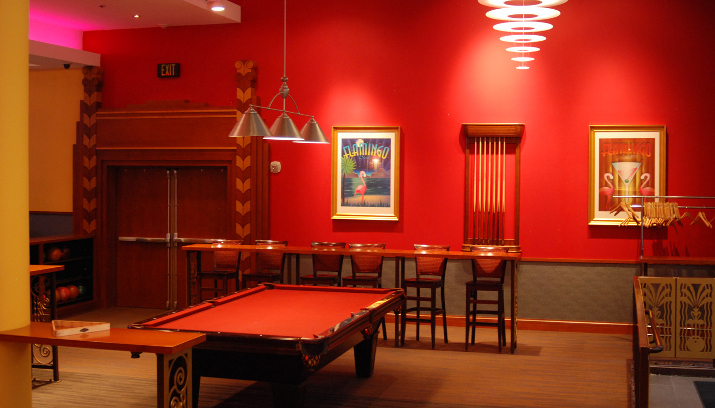 Red pool table in the Palm Room under an art-deco chandelier, with framed art on the walls