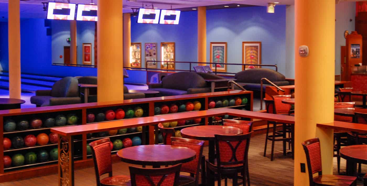 Colorful bowling balls on a wood rack with cocktail tables in front