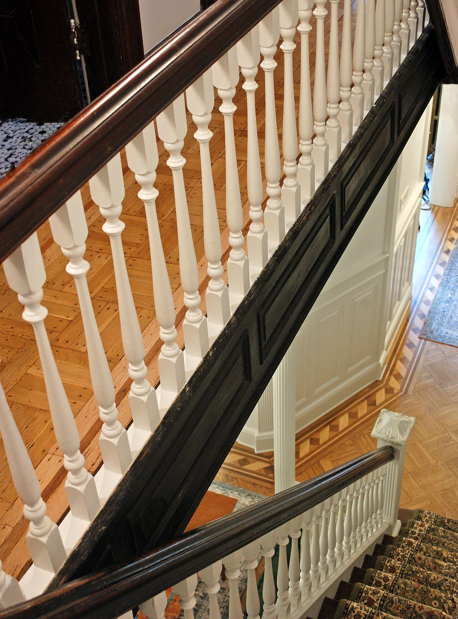 Wooden staircase with dark handrails, white balusters, patterned carpet, and parquet flooring.