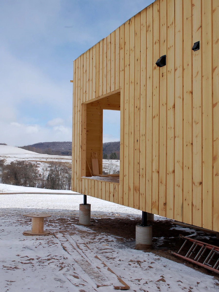 Partially constructed wooden building elevated on concrete piers, with snow on the ground.