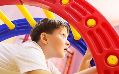 Young boy playing on colorful gym climbing equipment indoors.