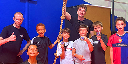 At the Ventura Ninja Challenge some boys hold medals and one boy holds a trophy, one man gives a thumbs up.