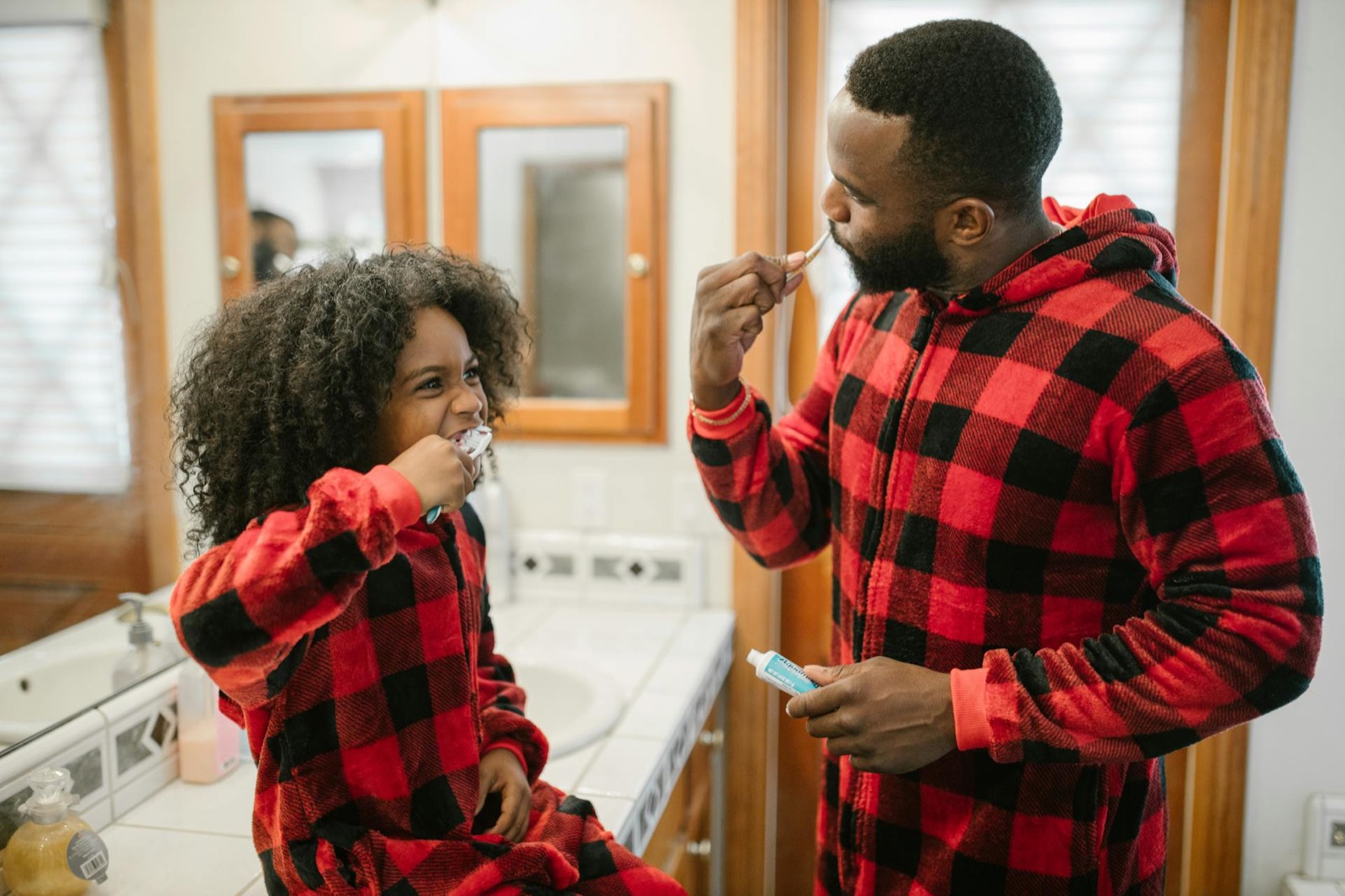 Father and daughter brushing teeth together in matching red plaid pajamas