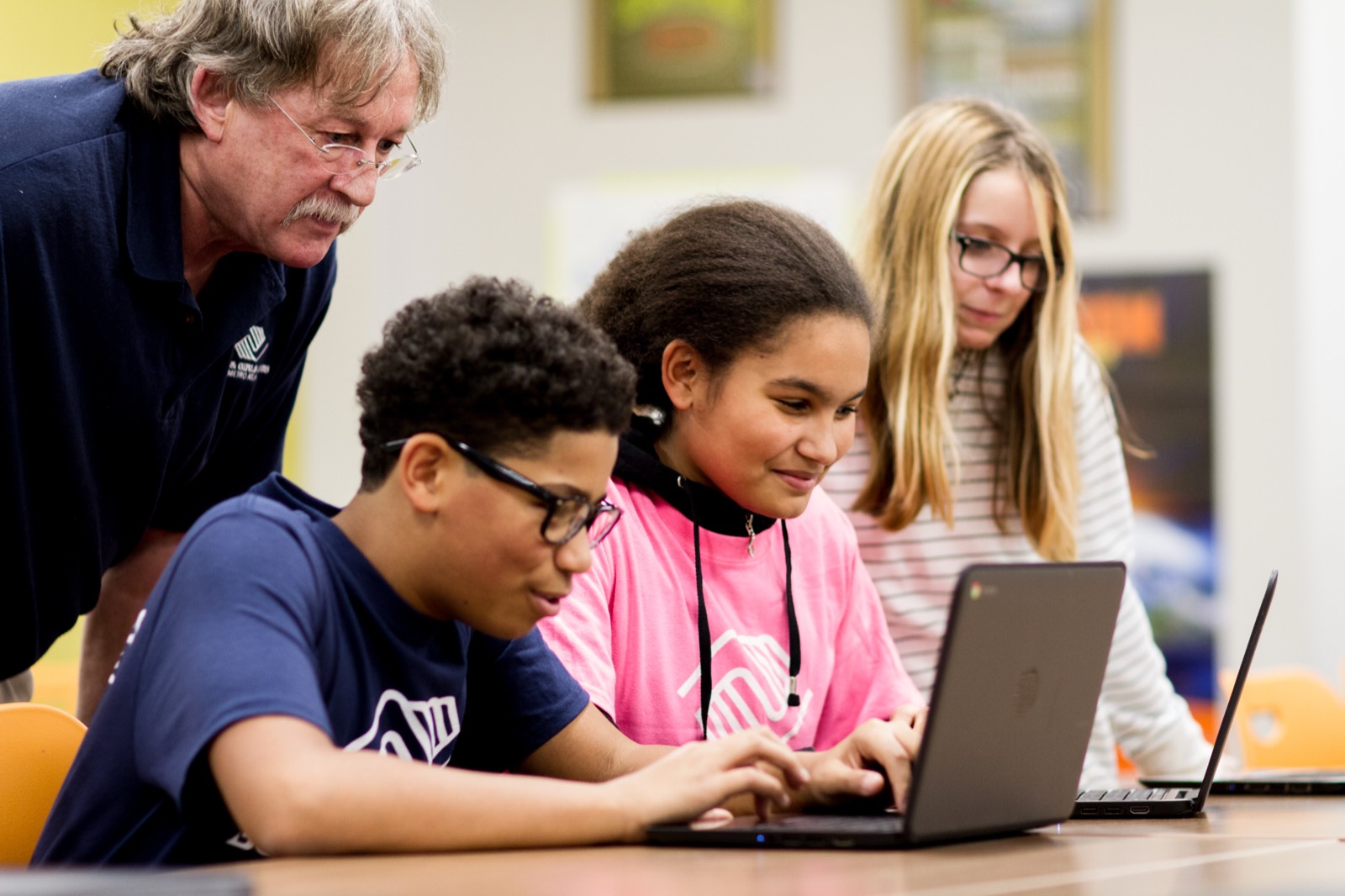 Club staff member helping three young people work on a laptop