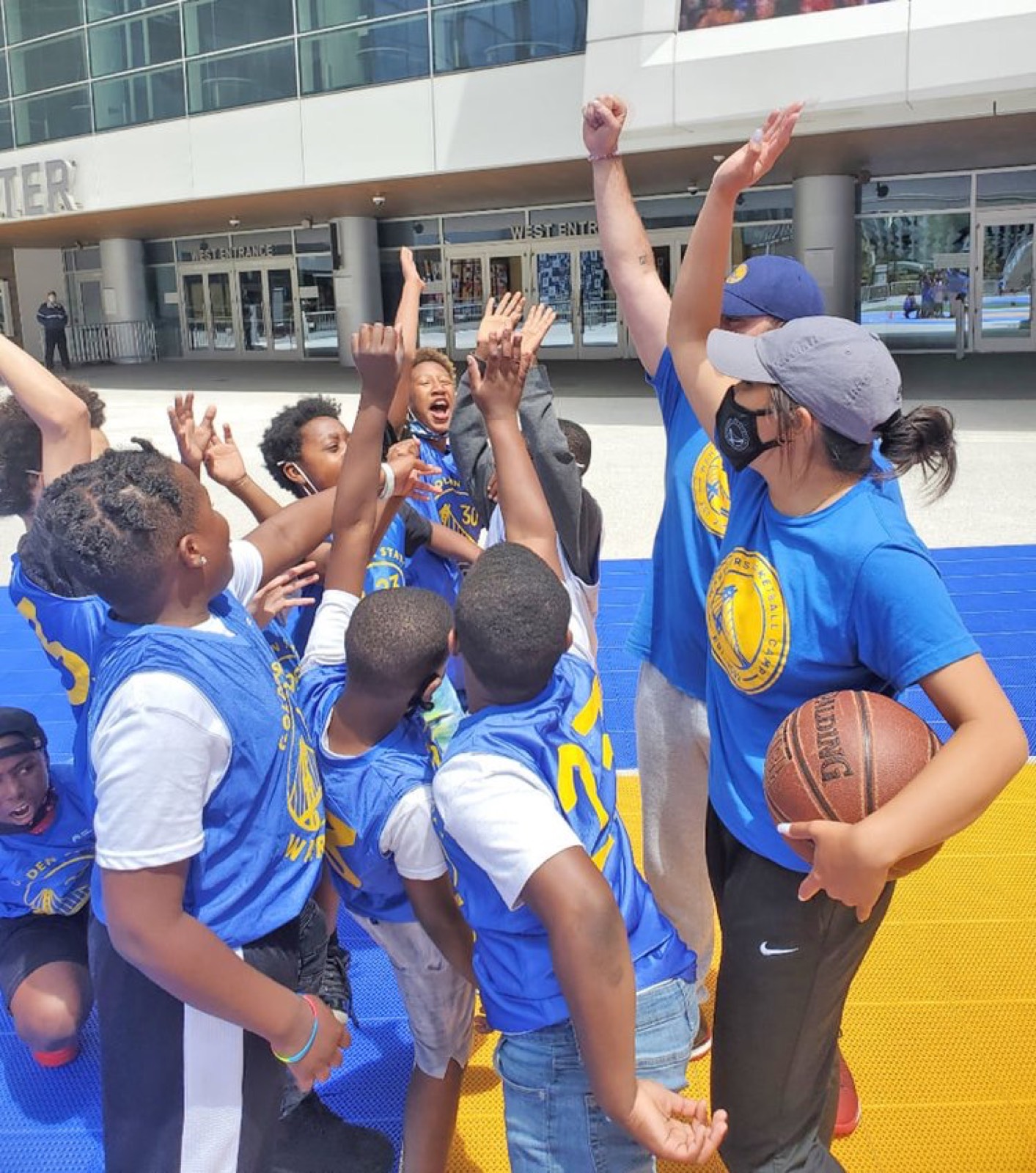 Kids in blue jerseys cheering with their arms raised on a basketball court