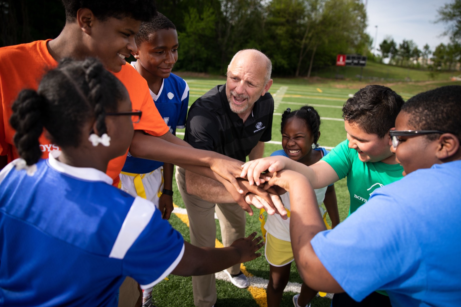 A Club staff member and young people stacking their hands together in a huddle on an outdoor football field