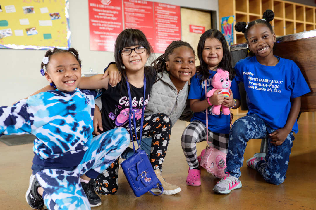 Five smiling Boys & Girls Clubs of Oakland girls posing close together on the floor of a clubhouse