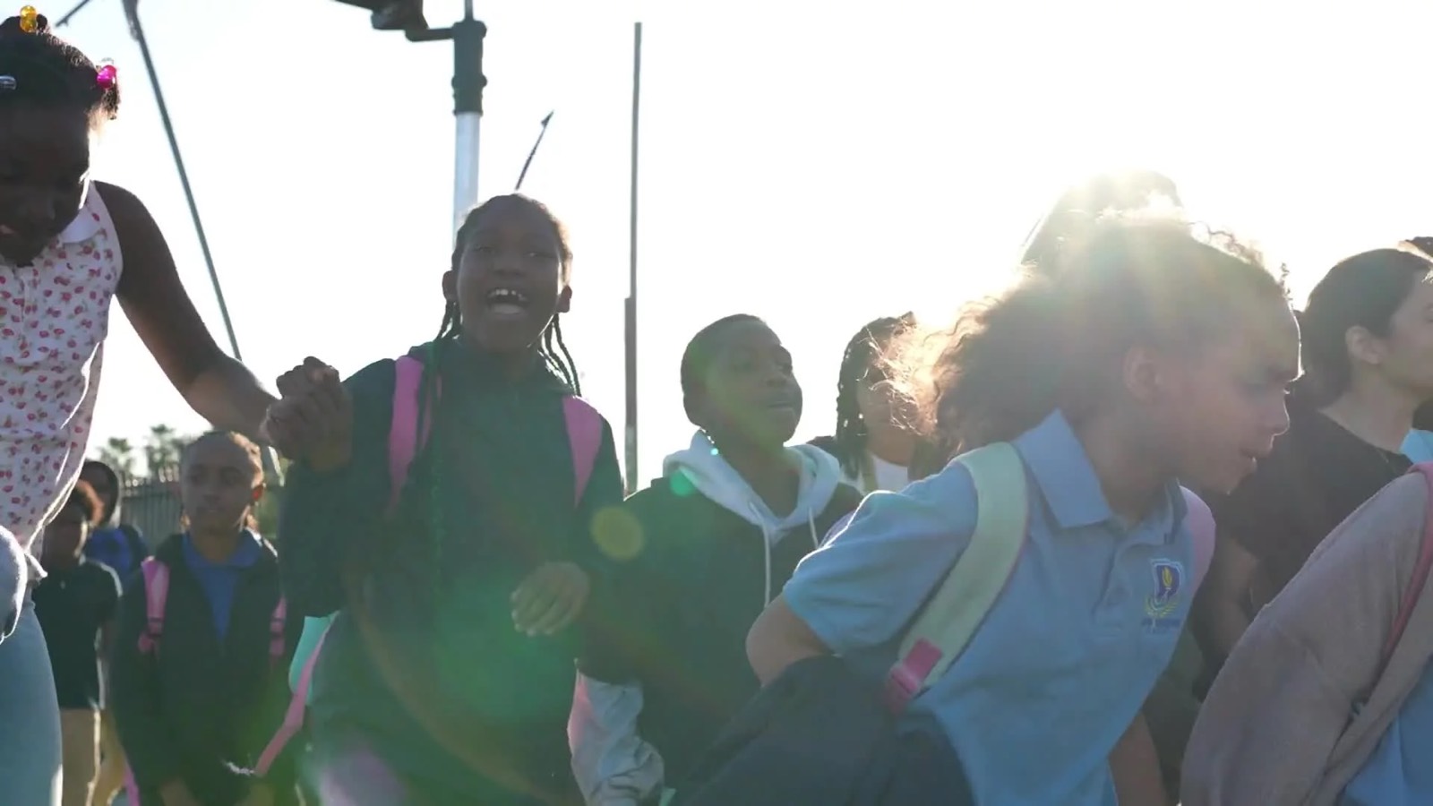 Smiling schoolchildren with backpacks walking together in bright sunlight, two holding hands