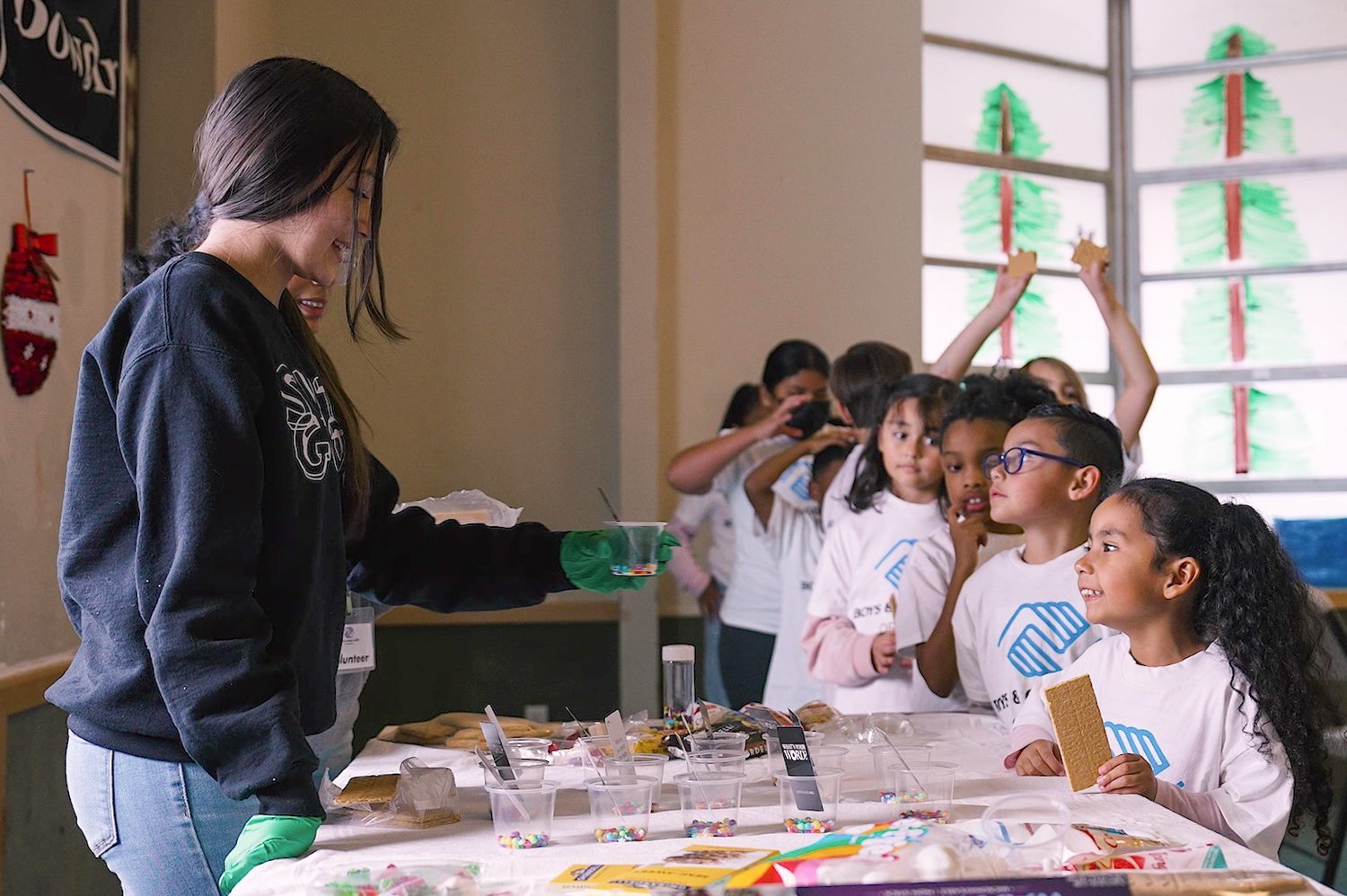A teen staff member serving treats to younger Club members in white Boys & Girls Clubs T-shirts at a craft table