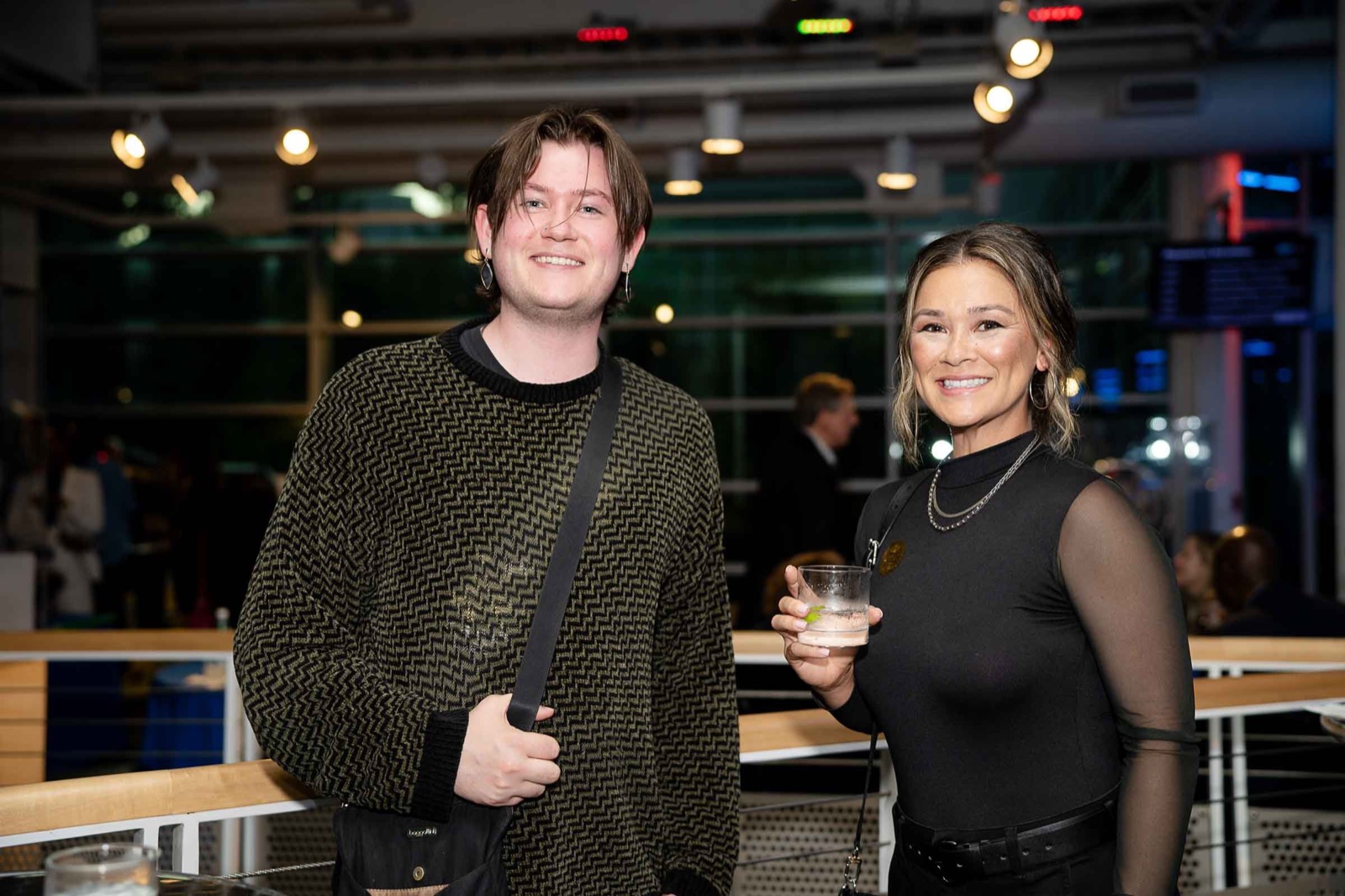 Two young guests posing together in the exhibit hall at the gala, one holding a drink