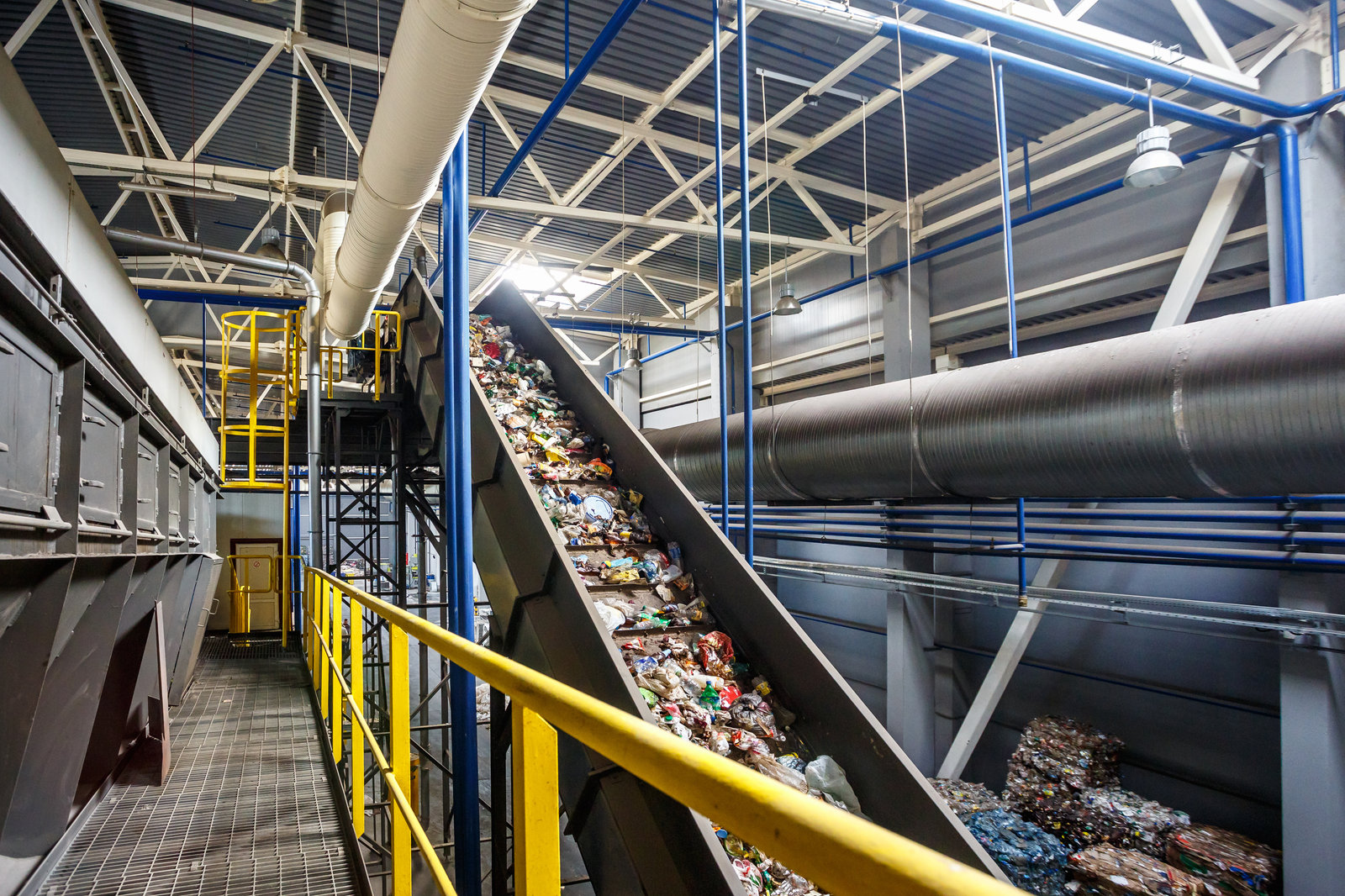 Convoyeur incliné transportant des déchets plastiques dans un centre de tri, à côté de balles compressées