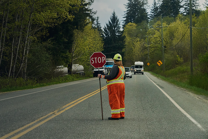 Certified flagger holding a STOP sign on a rural road as vehicles approach