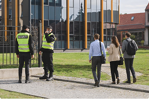 Two security guards in hi-vis vests outside an office building as pedestrians walk past
