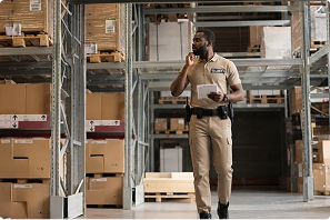 Security guard with a tablet and radio walking a warehouse aisle