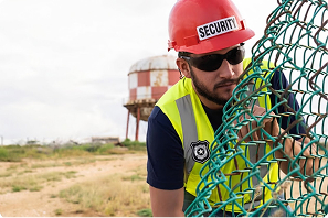 Security guard in a hard hat and hi-vis vest inspecting a construction site fence