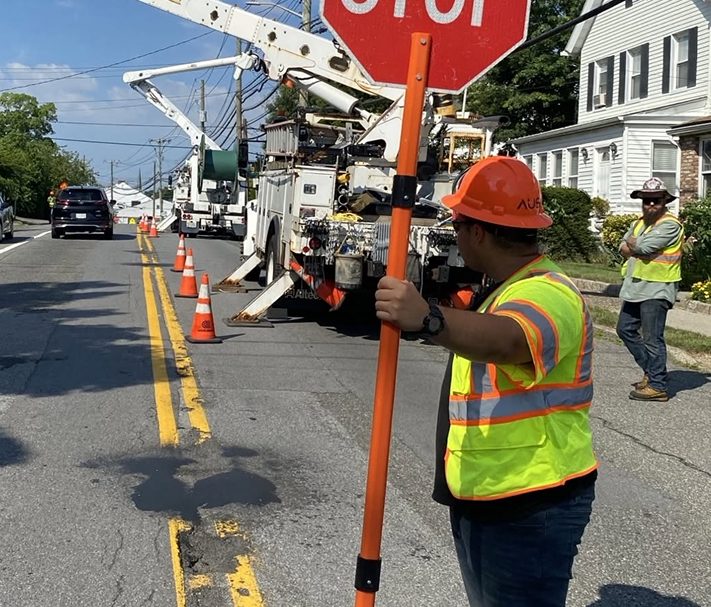 Flagger holding a STOP sign in front of utility trucks working on a roadway