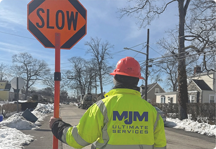 MJM Ultimate Services flagger holding a SLOW sign on a snowy suburban street