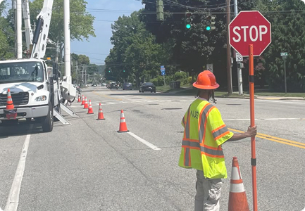 Flagger in a hi-vis vest holding a STOP sign next to a utility bucket truck on a residential street