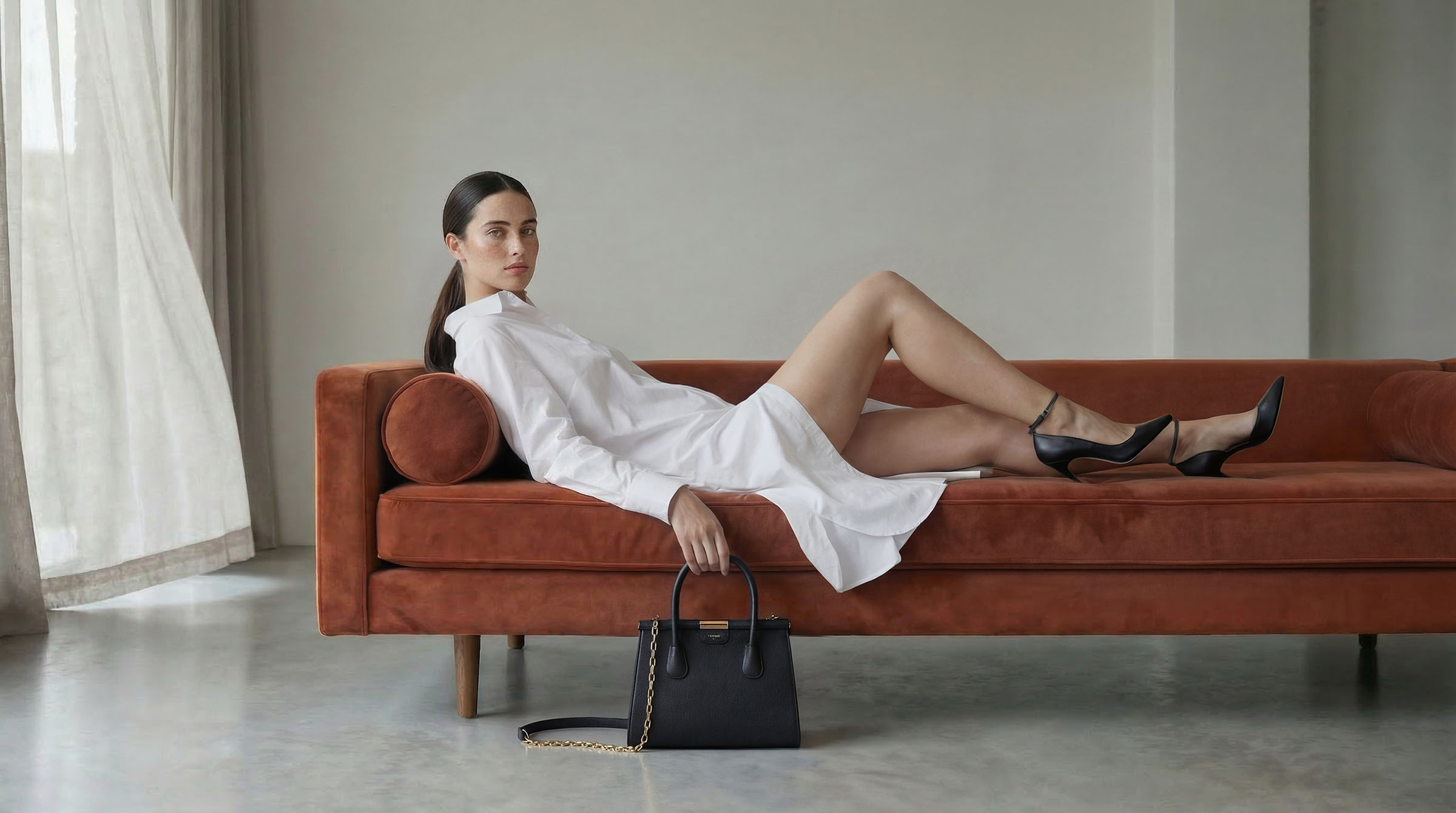 AI fashion editorial: model in a white shirt on a rust velvet sofa with a Moncrief handbag