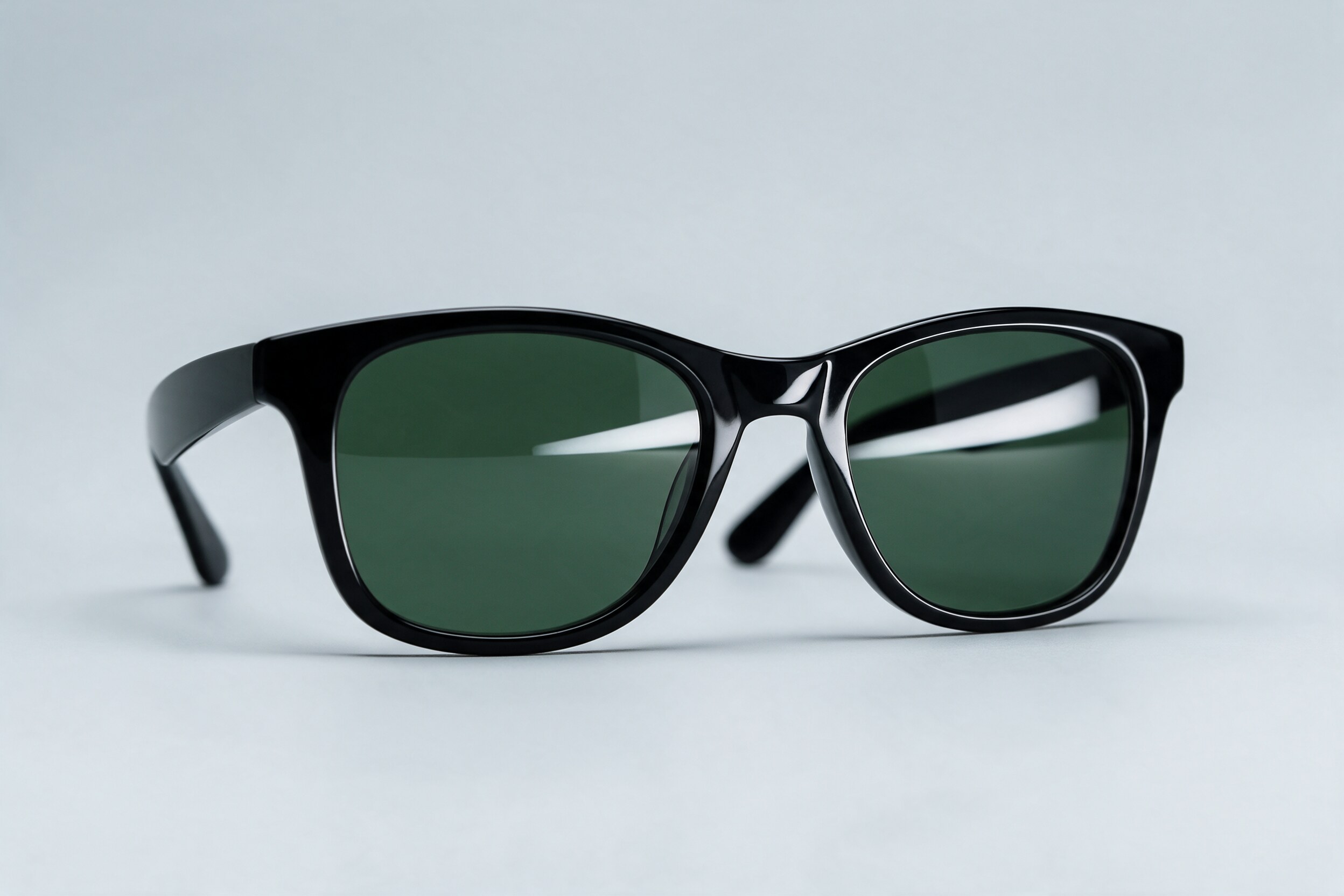 Black acetate sunglasses with green lenses on a pale grey background, with one clean softbox reflection on each lens
