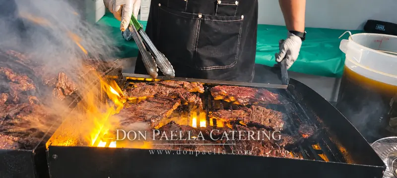 Cook tending steaks above flames at a grilling station