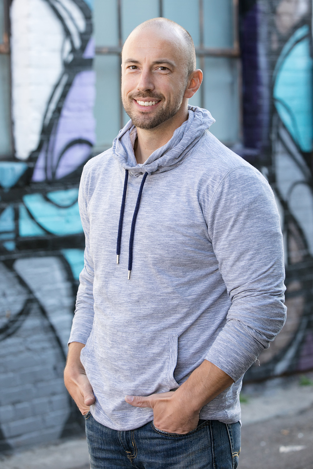 Justin Kraft in a grey hoodie in front of a mural