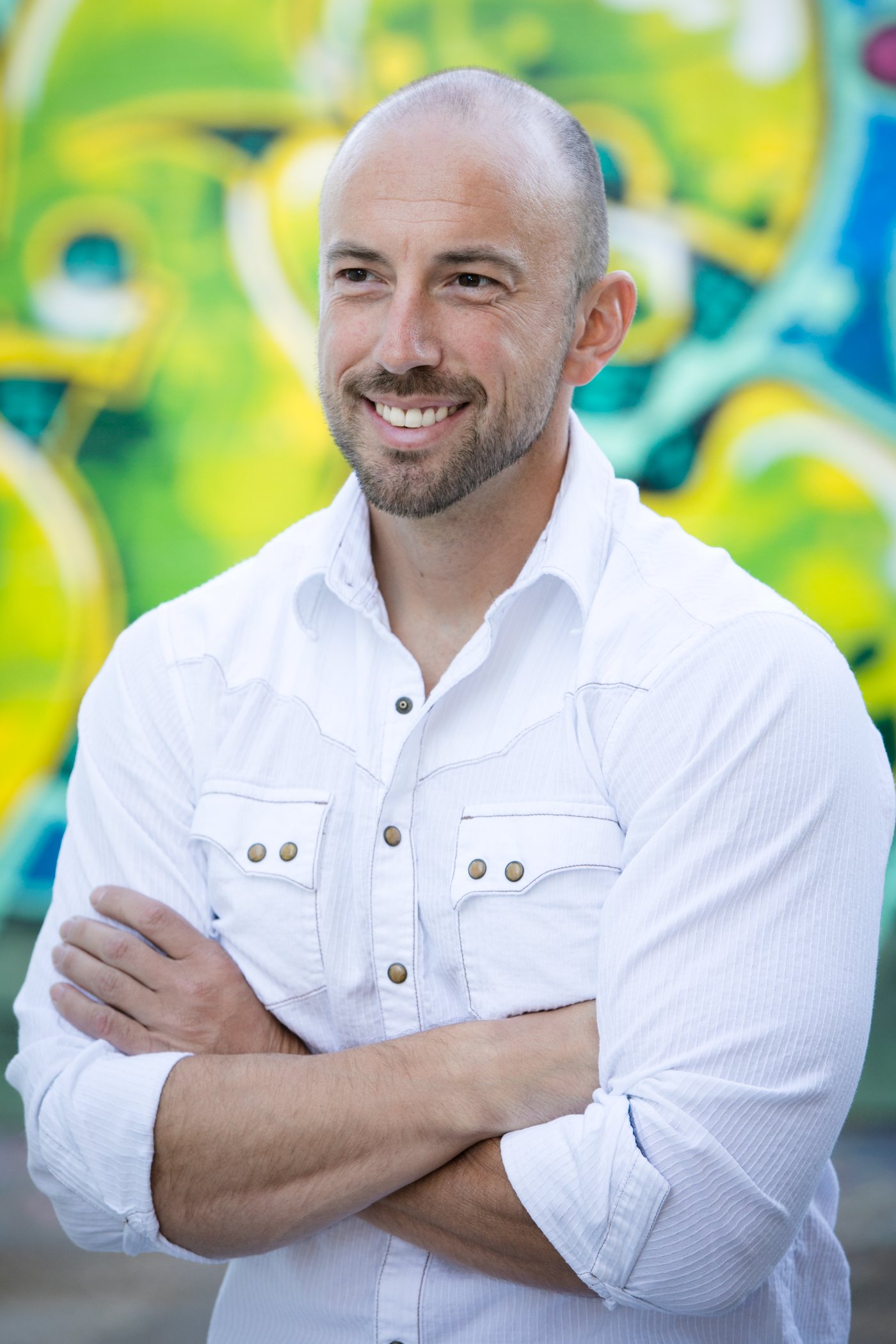 Justin Kraft with arms crossed in front of a green and yellow mural
