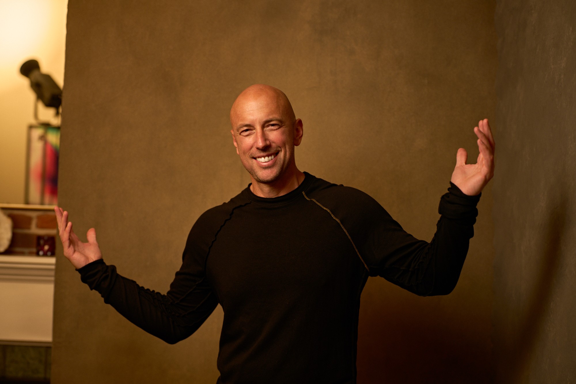 Justin Kraft smiling with both hands raised, in front of a bronze textured wall