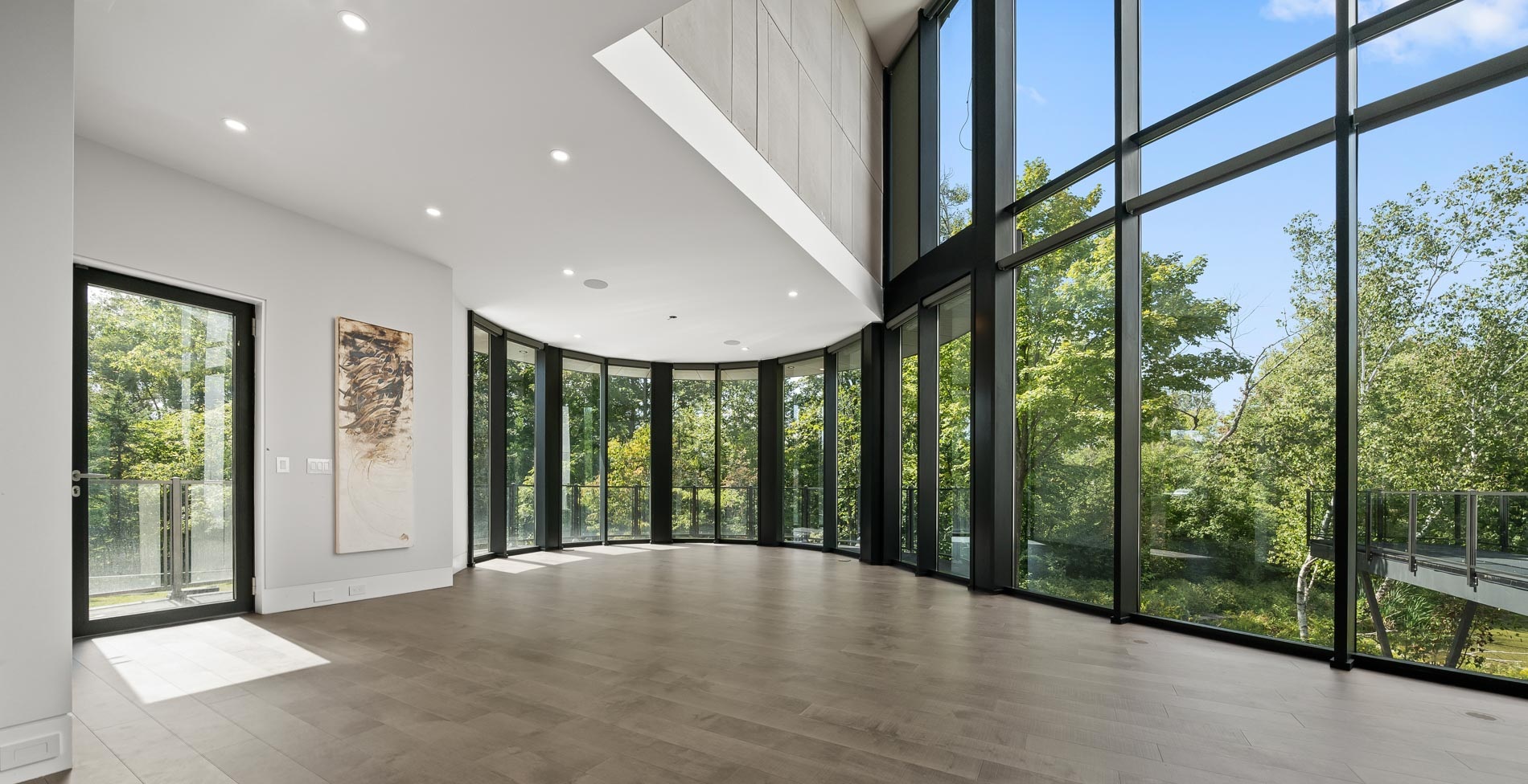 Double-height aluminum curtain wall and curved window wall glazing in a contemporary home overlooking trees