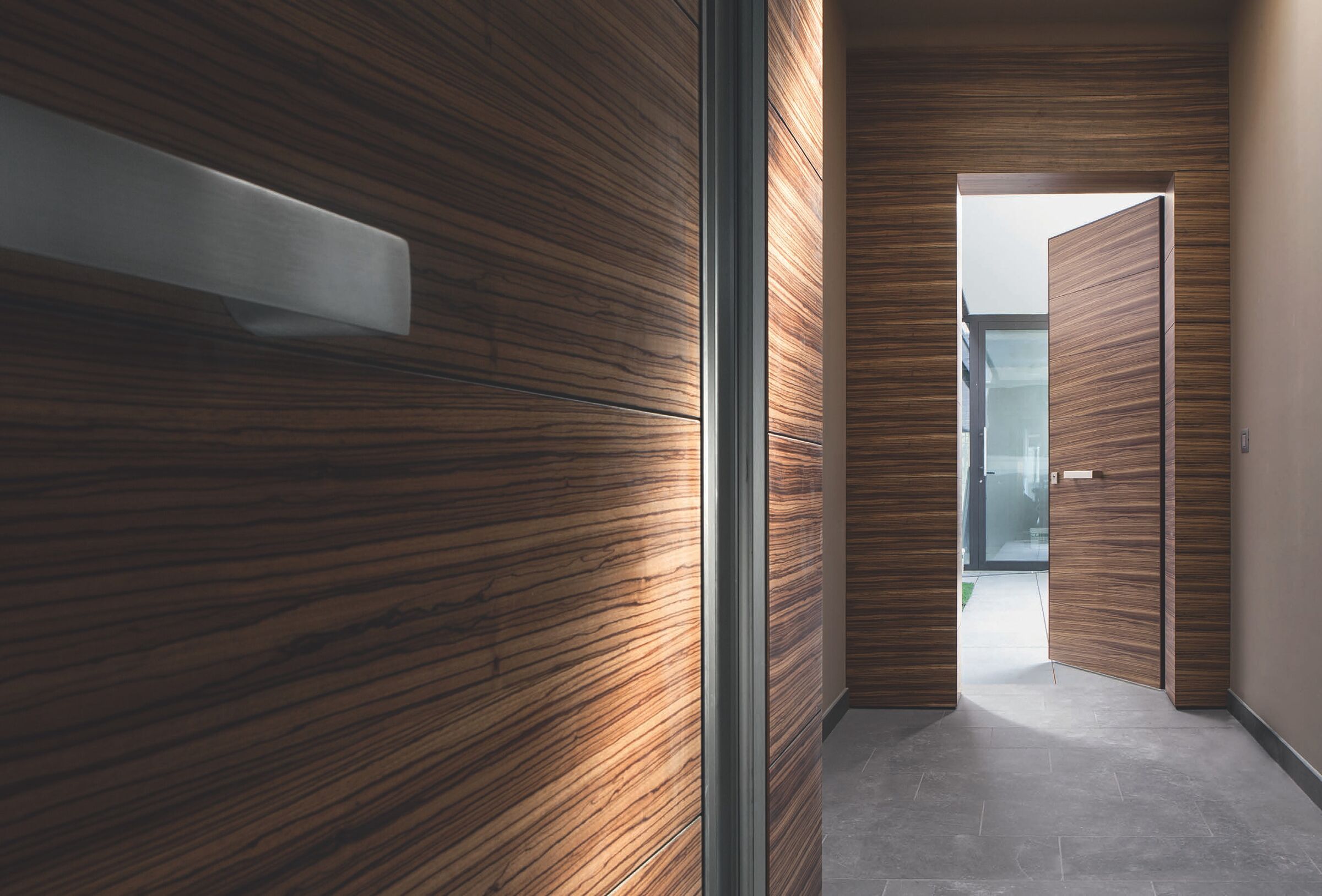 Flush entrance door clad to match a wood-paneled wall, opening to a hallway