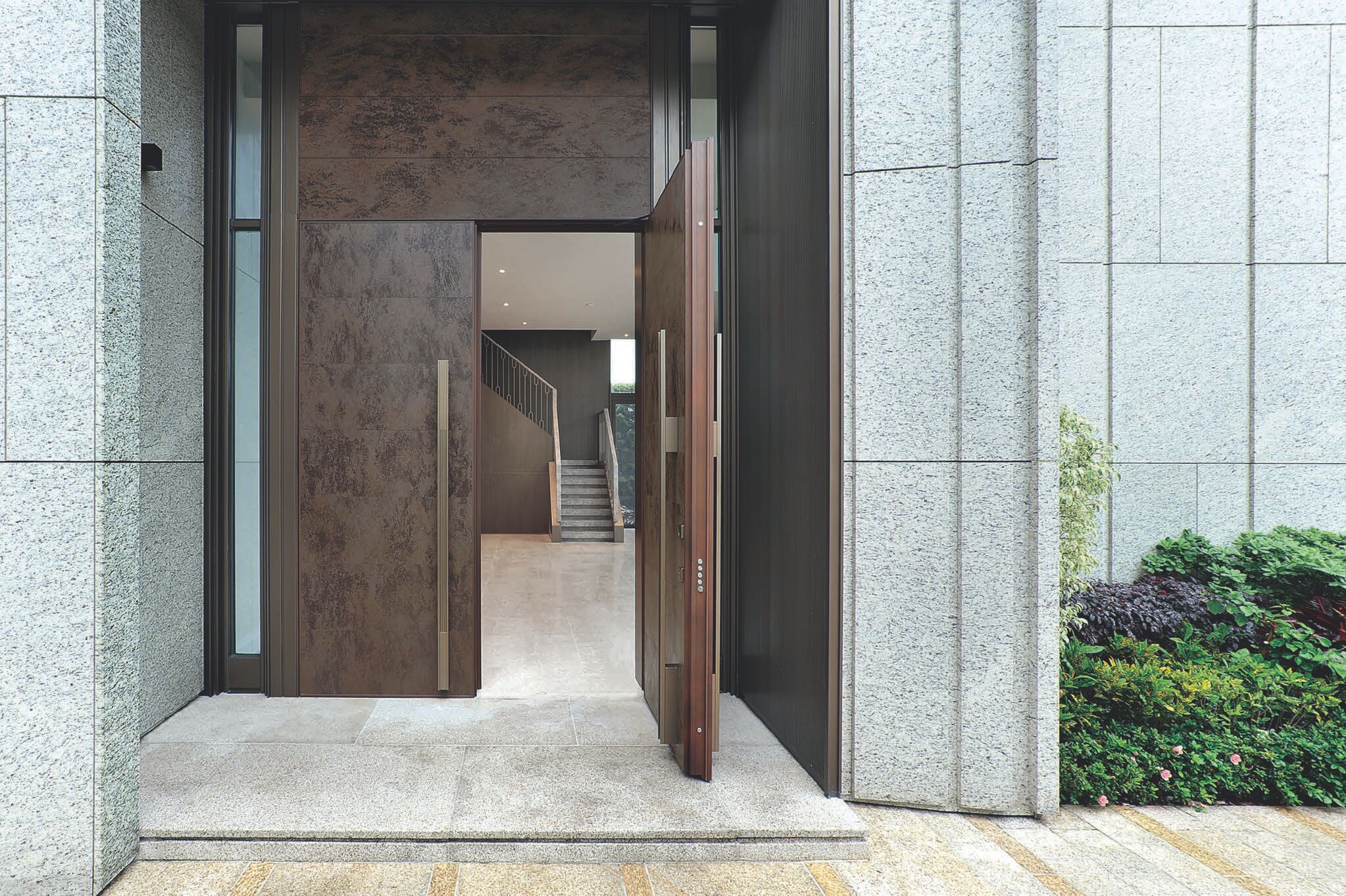 European-style entrance door clad in rust Cor-Ten ceramic with a long handle under a transom