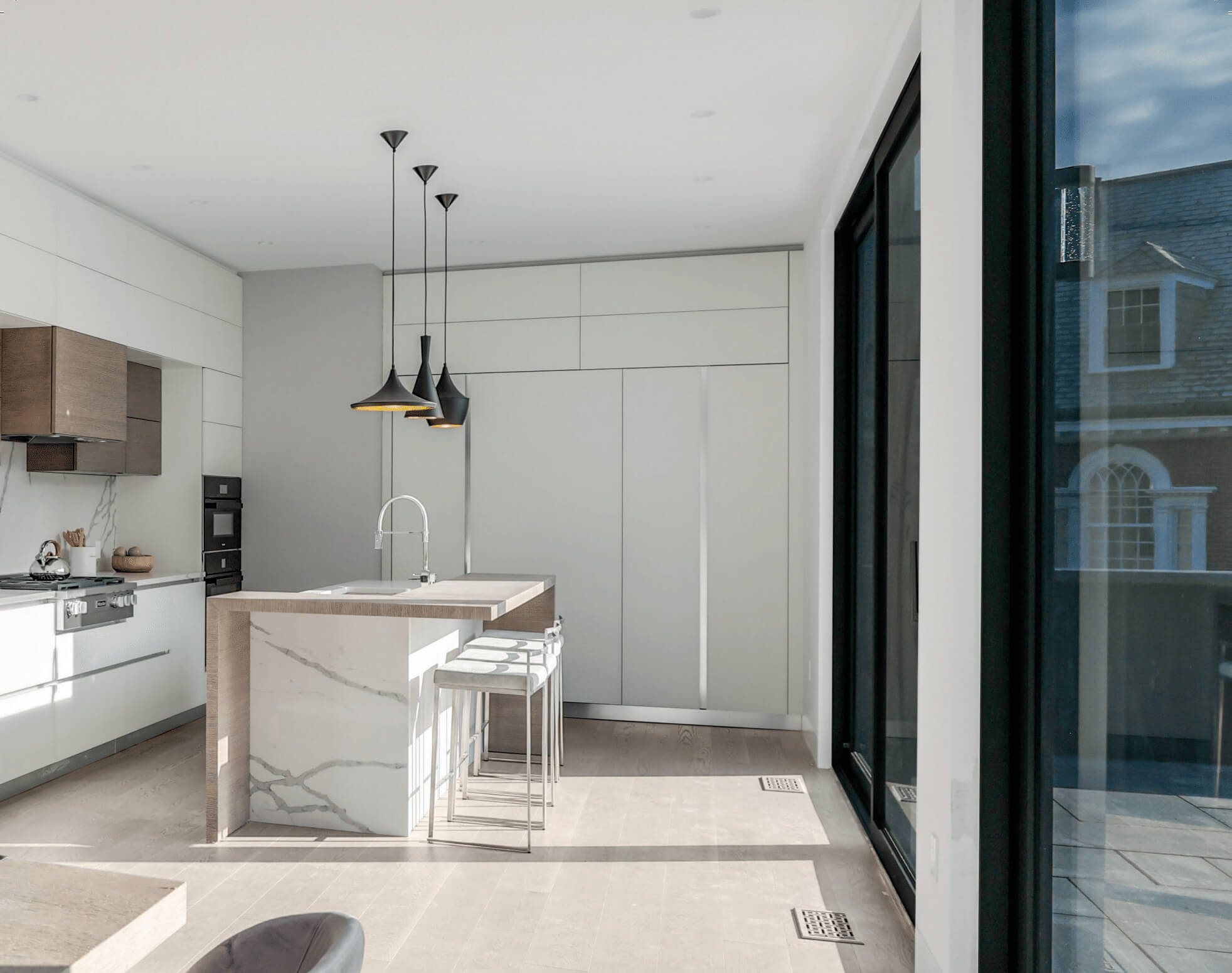 Kitchen island beside a full-height dark-framed Westline glass door in a modern Brookline, MA villa