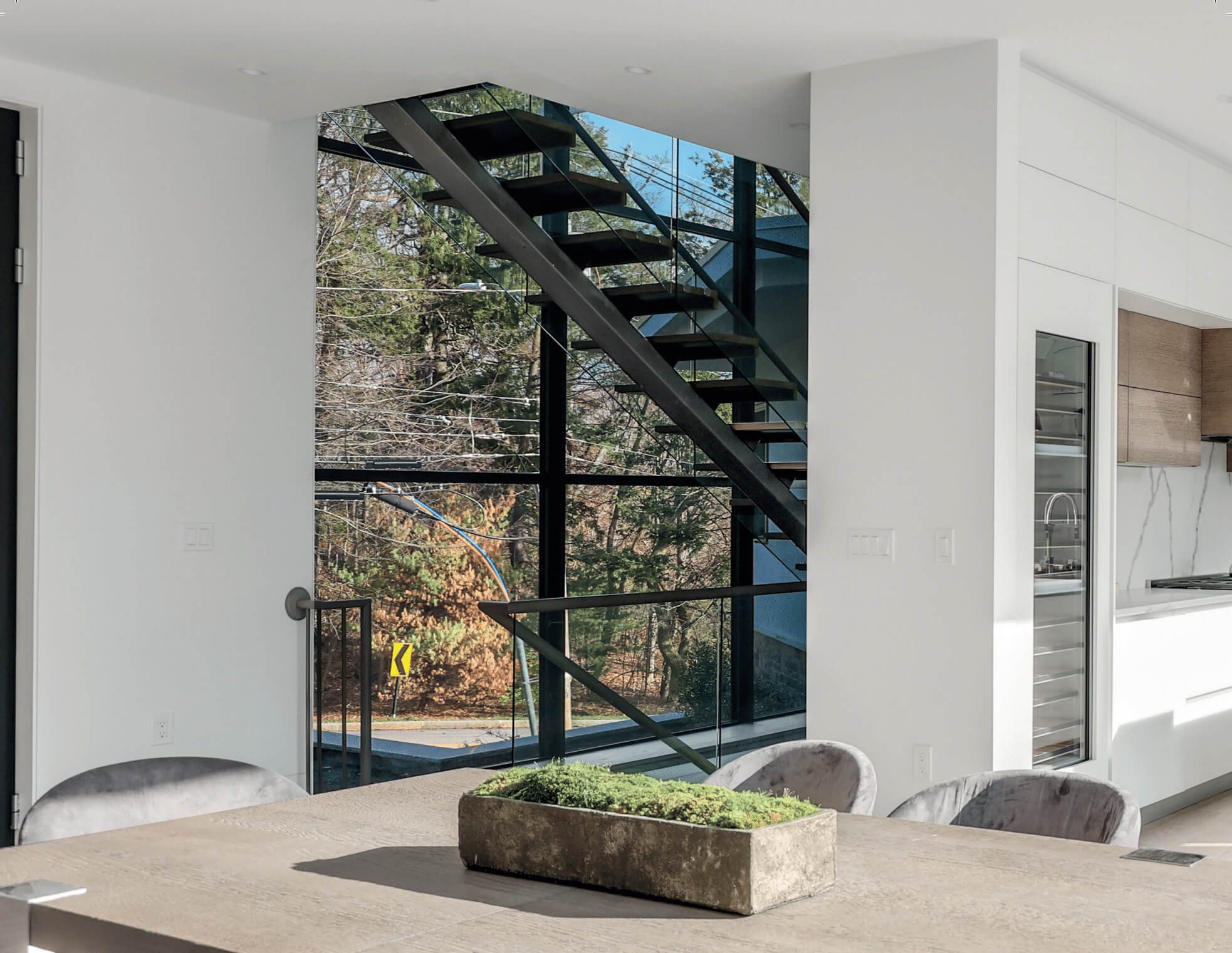 Dining area and open staircase in front of a tall dark-framed Westline glass wall in a Brookline, MA villa