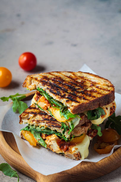 Grilled panini sandwich with melted cheese, spinach, and roasted tomatoes on parchment paper.