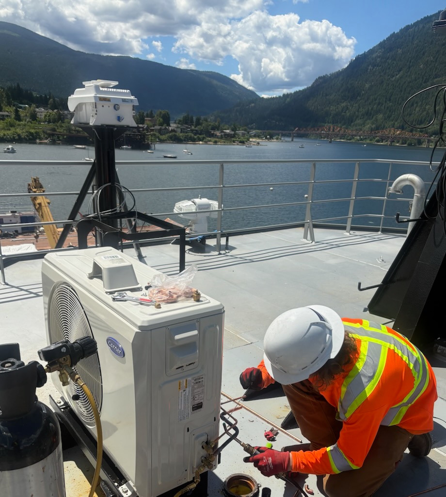 Technician working beside an outdoor unit on a vessel deck during the BC Ferries project.