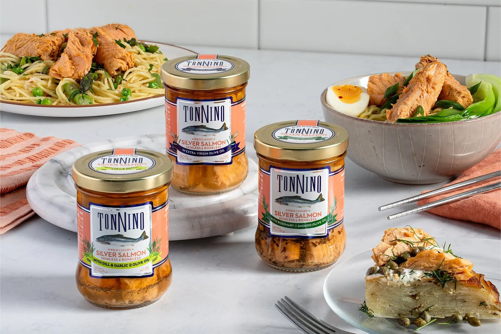 Jars of Tonnino wild-caught silver salmon styled with pasta and noodle bowls on a kitchen counter