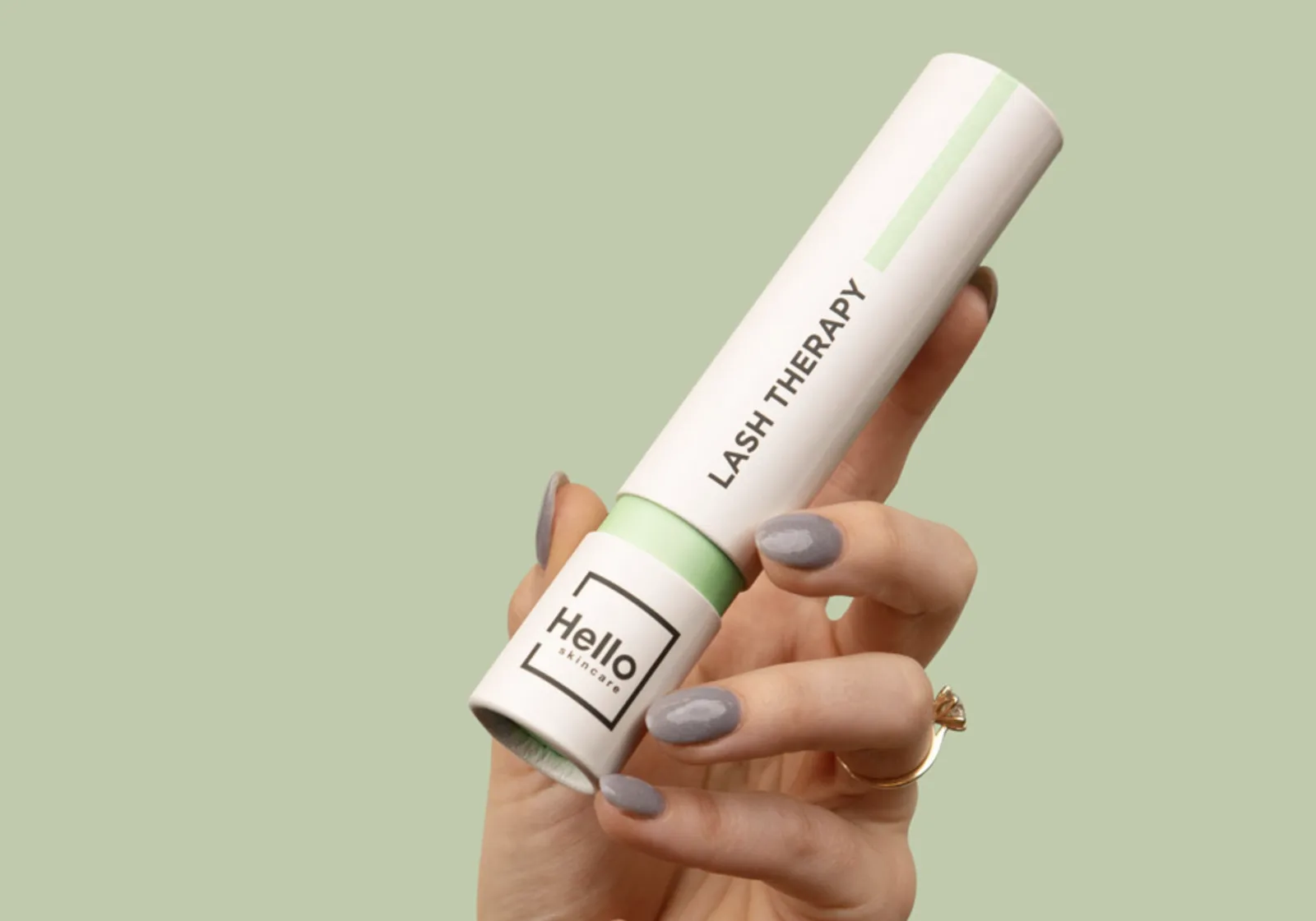A hand holding a Hello Skincare lash therapy tube against a sage green background