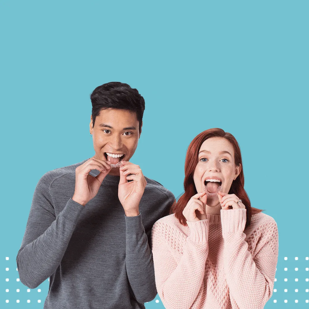 A smiling man and woman each holding a clear dental aligner to their teeth against a blue background
