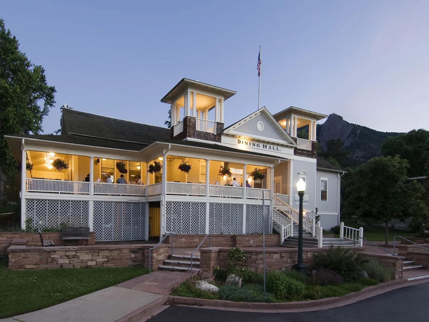 The Colorado Chautauqua dining hall lit up at dusk with a Flatirons peak rising behind its wraparound porch