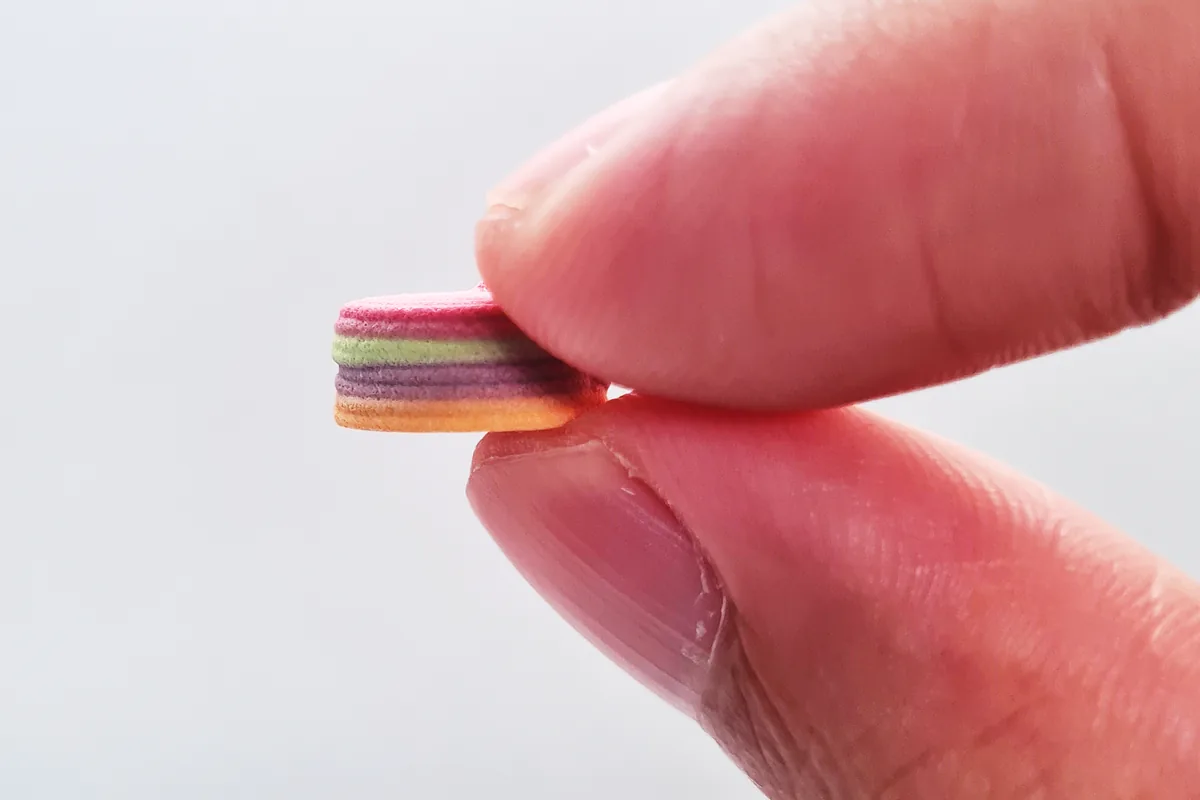 CraftTab 4-in-1 polypill, a multi-layer 3D-printed tablet, held between two fingers