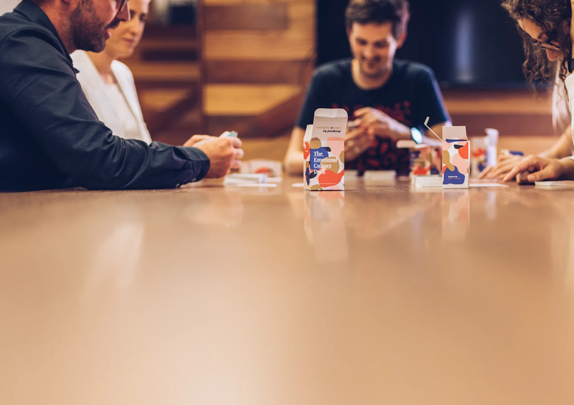 A hand holding two Emotional Culture Deck cards: Our success relies on our people feeling this, and We absolutely don't want our people to feel this
