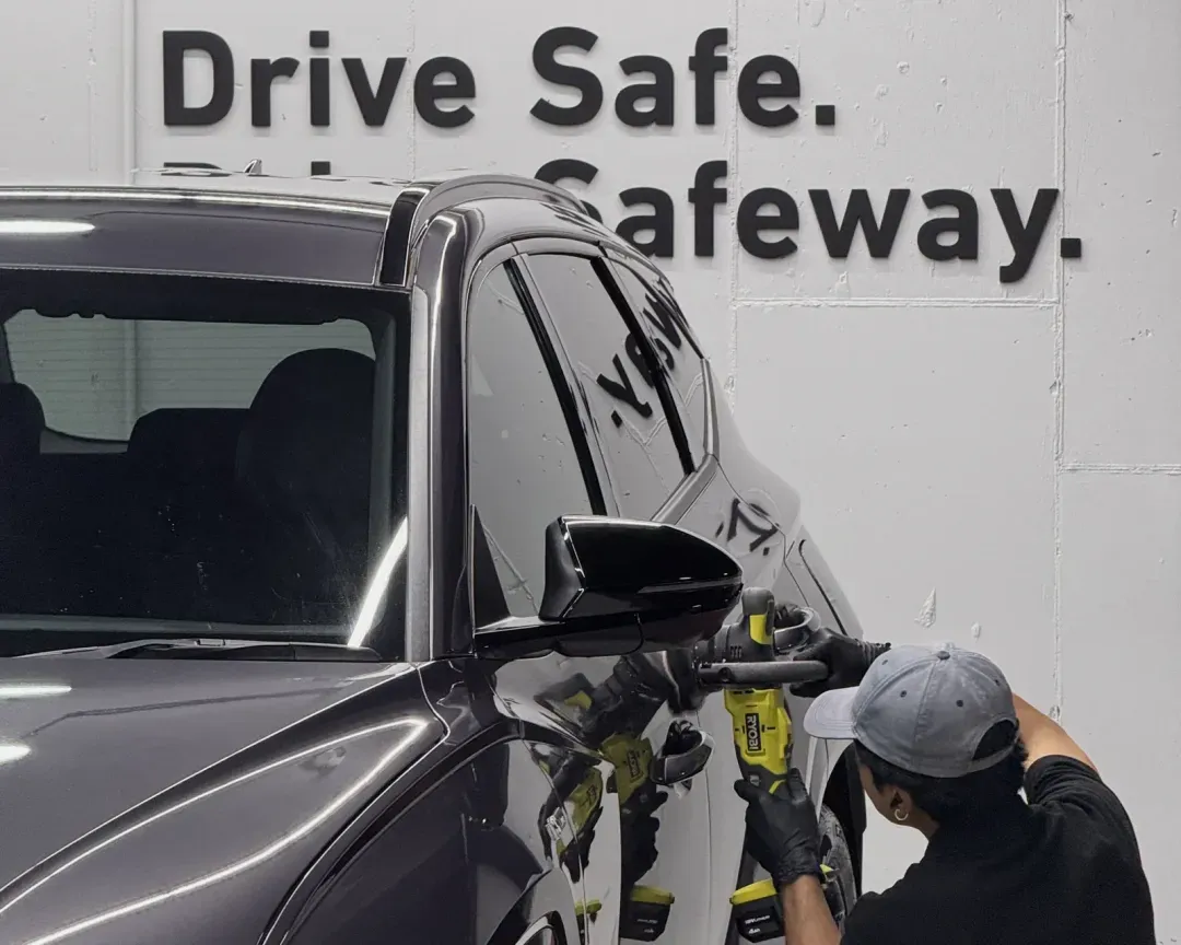 A Safeway Auto technician machine-polishing a dark SUV during vehicle preparation in the West End showroom