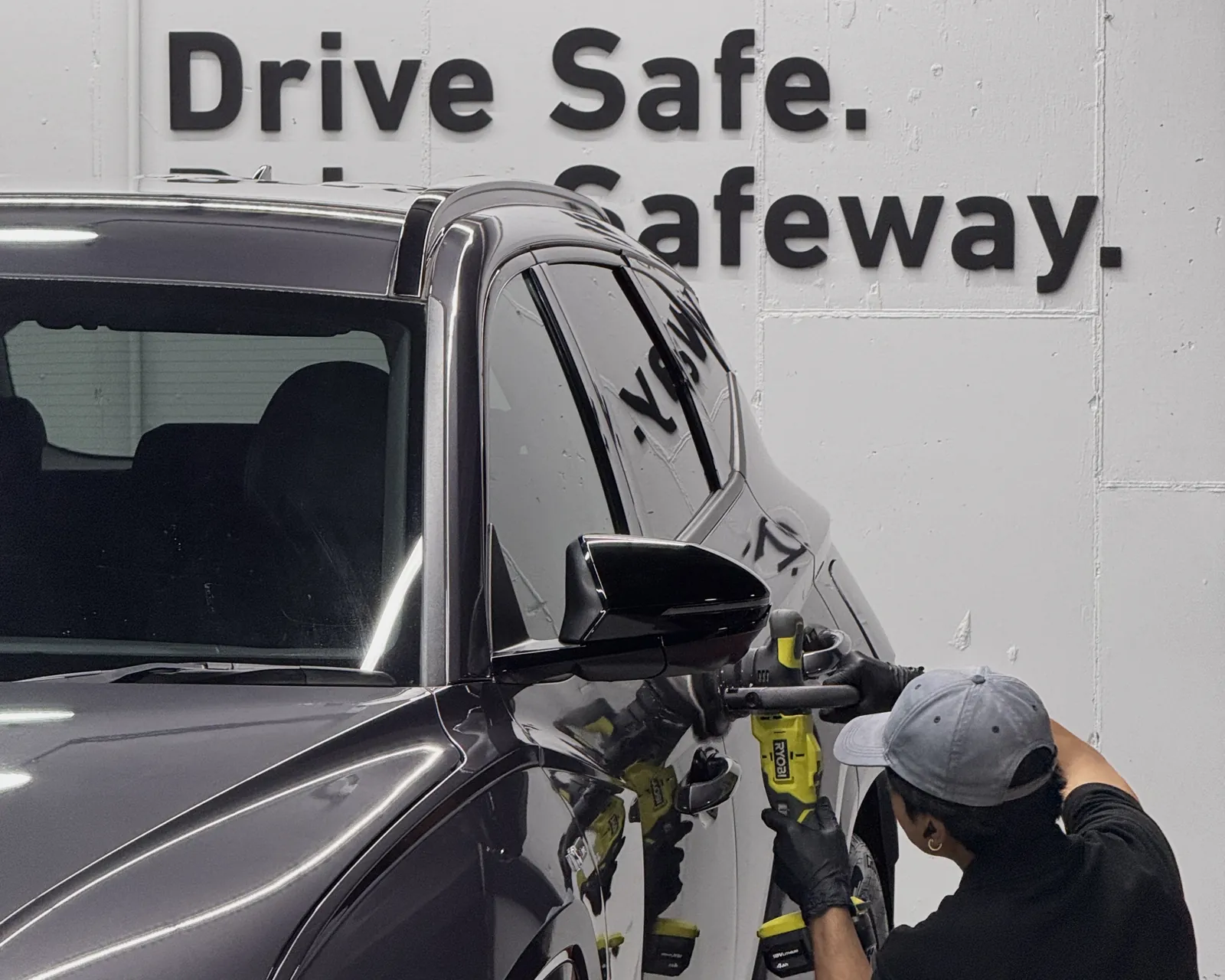 A Safeway Auto technician machine-polishing a dark SUV in the workshop, beneath the Drive Safe. Drive Safeway. wall lettering