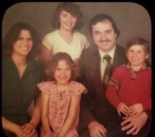 A vintage family portrait from Angie’s family album, with two adults and three children.
