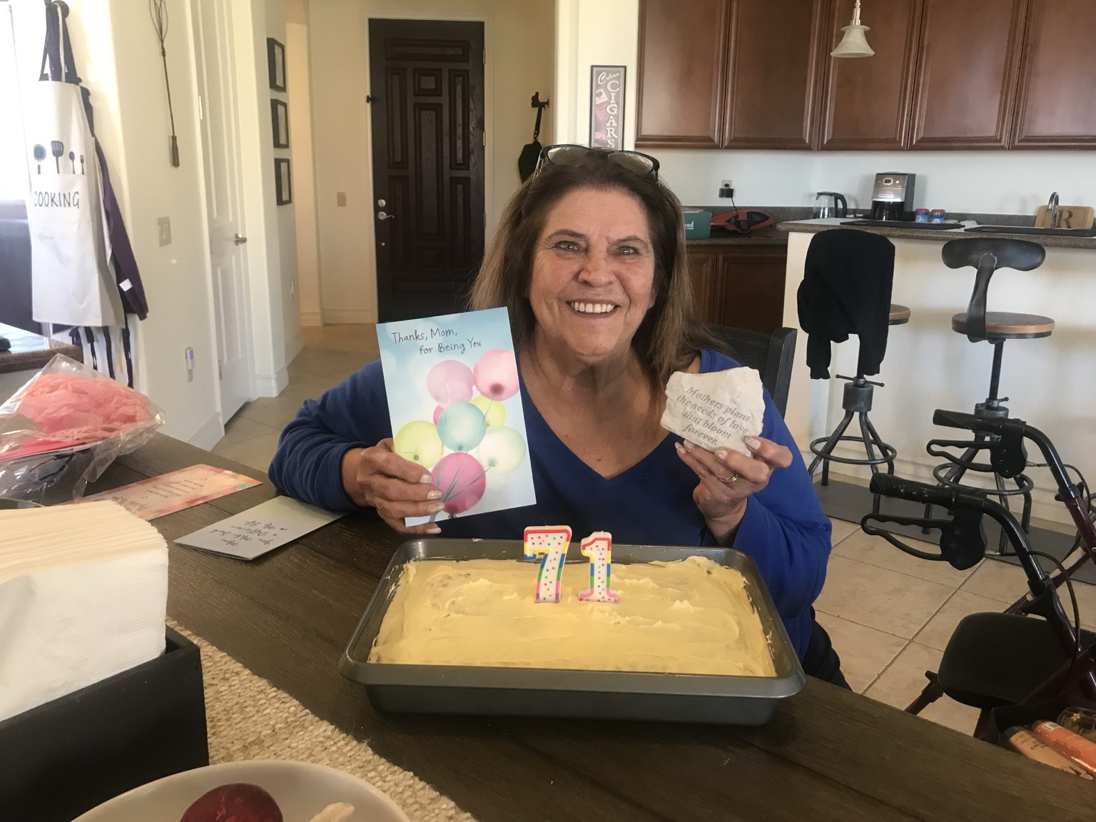 Angie’s mother smiling behind a cake with 71 candles, holding a card and a keepsake.