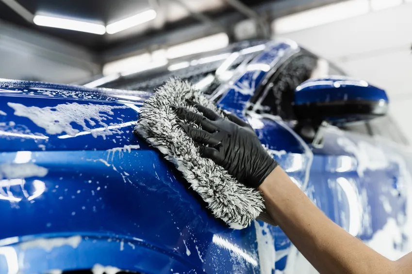 A microfiber wash mitt cleaning the bodywork of a blue car