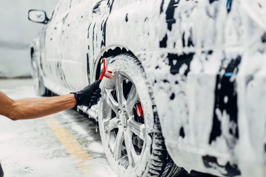 A small detailing brush cleaning a foamy alloy wheel