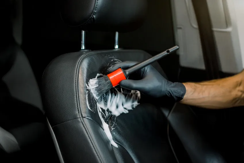 A gloved detailer brushing foam onto a vehicle seat